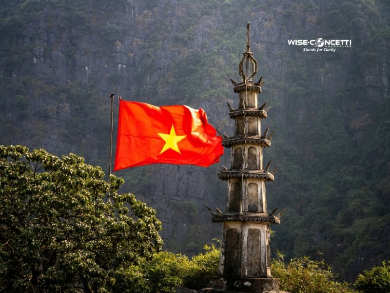 Vietnamese national flag flying beside an ancient stone tower, representing the country's cultural and linguistic heritage